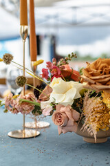 Wedding decor in blue. Banquet tables with tablecloths are decorated with compositions of flowers, on the tables are plates, glasses and candles
