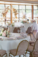 Wedding decor in pink. Banquet tables with tablecloths are decorated with compositions of flowers, on the tables are plates, glasses and candles
