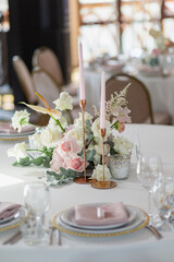 Wedding decor in pink. Banquet tables with tablecloths are decorated with compositions of flowers, on the tables are plates, glasses and candles

