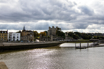 Rochester Castle, from the bridge across the Medway River.  Storm clouds were gathering but the sun was still shining.  Sunbeams are seen through the clouds.  October 2021.