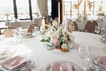 Wedding decor in pink. Banquet tables with tablecloths are decorated with compositions of flowers, on the tables are plates, glasses and candles
