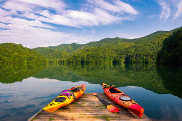 Kayaks on dock with mountains reflecting on calm water in the background - obrazy, fototapety, plakaty