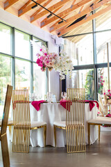 Elegant banquet table set with glasses decorated with gold, lit candles and pink flowers
