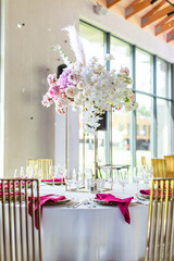 Elegant banquet table set with glasses decorated with gold, lit candles and pink flowers
