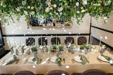 Banquet table is decorated with plates, cutlery, glasses, candles and flower arrangements. Wedding decor