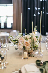Banquet table is decorated with plates, cutlery, glasses, candles and flower arrangements. Wedding decor