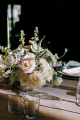 Banquet table is decorated with plates, cutlery, glasses, candles and flower arrangements. Wedding decor