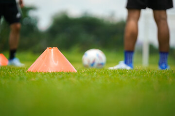 An orange obstruction cone on the firm grass ground with football player in training action as...