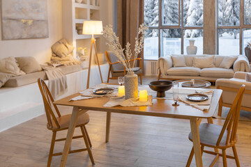 cozy warm home interior of a chic country chalet with a huge panoramic window overlooking the winter forest. open plan, wood decoration, warm colors and a family hearth