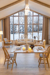 cozy warm home interior of a chic country chalet with a huge panoramic window overlooking the winter forest. open plan, wood decoration, warm colors and a family hearth
