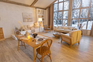 cozy warm home interior of a chic country chalet with a huge panoramic window overlooking the winter forest. open plan, wood decoration, warm colors and a family hearth