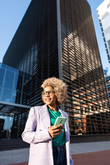 Modern cheerful african american executive business woman outside the workspace office, holding a smartphone