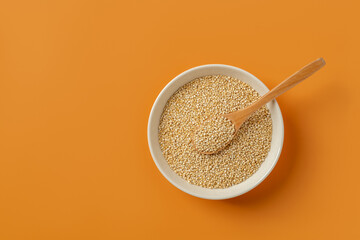 White quinoa seeds and wooden spoon in a beige bowl over orange background. Chenopodium quinoa for superfood concept. Raw quinoa grains for gluten free dieting. Vegetarian eating. Copy space.
