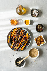Baked glazed spicy violet and orange carrots with ingredients on grey background. Top view
