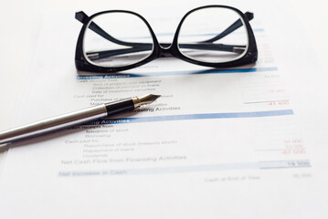 Work desk, documents, pen, glasses on a white table.