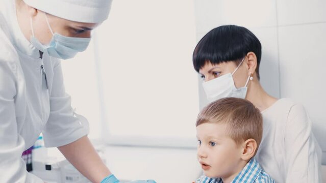 little boy is taking blood from a vein for analysis. The child sits in the arms of his mother in the manipulation room of the clinic.