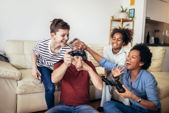 Smiling family enjoying time together at home sitting on sofa in living room and playing video games.