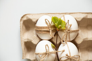 Fototapeta na wymiar Chicken eggs tied with a rope lie in an egg tray and a tree branch with green leaves, Easter holiday in Ukraine, decorate eggs for the holiday