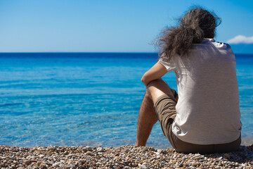 Man is sitting lonely from the back and looking to the Mediterranean blue sea. Horizontal.