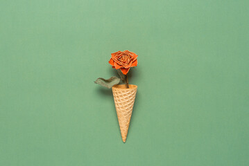 Dried rose in a waffle cone on a green pastel background. Top view, flat lay. Creative layout.