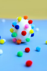 Egg with colorful pom-poms and scattered pom-poms, side view