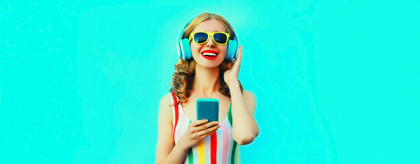 Portrait of happy smiling young woman listening to music in headphones with smartphone on blue...