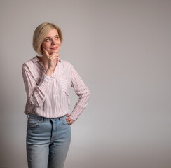 Thoughtful young woman touching chin, looking aside at copy space, attractive female pondering deal, pensive client customer thinking about shopping offer, isolated on grey studio background