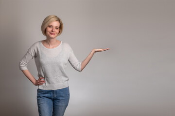 Portrait of stylish, nice, cute, modern woman in denim, casual outfit having empty place, copy space on her palm, looking at camera, on grey background