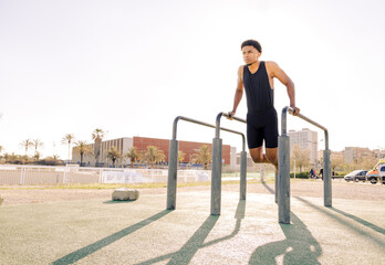 Dips exercise. Young guy doing calisthenics exercises. Outdoor training and working out.  - obrazy, fototapety, plakaty