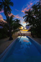 Idyllic sunset beach scene, infinity pool in luxury resort, tropical landscape with palm trees and...