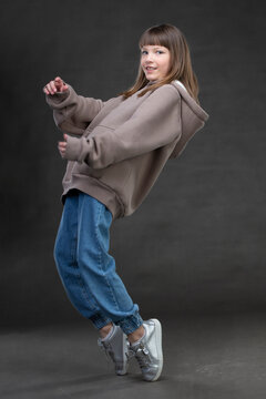 Beautiful teen girl in a sweatshirt and..jeans dances in front of the camera on a gray background.