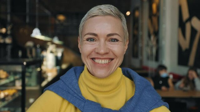 Mature woman smiling sincerely on camera at cozy cafe