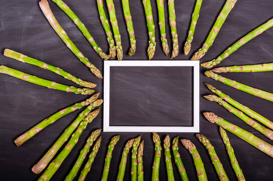 Stalks of fresh green asparagus around a white frame with a place for text on a black background.