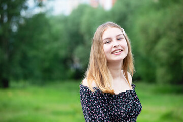 Fototapeta premium Happy young girl in a romantic dress on a green summer meadow. Beautiful teen girl smiles and looks into the camera.