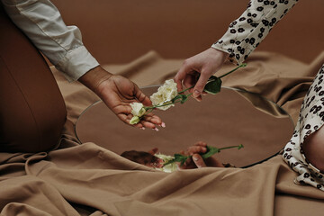 Close-up of young woman giving white flower to her girlfriend which reflected in mirror