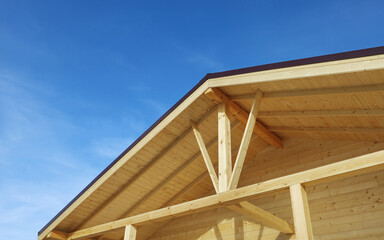 Roof design of wooden terrace house, textured surface and supporting beams, against blue sky 