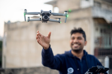 young indian male catching launching folding drone with camera from hand with controller in other hand smiling showing the rise of manufacturing and technology