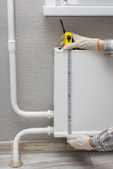 a man measures a heating radiator with a tape measure