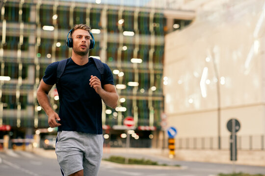 Young sporty man jogging through city streets with backpack on back