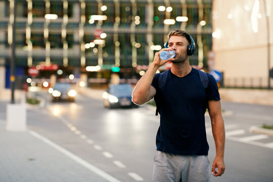 Young sports man making break and drinking water after jogging