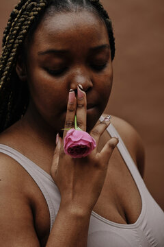 African young woman with braids holding pink rose in mouth and smoking it as cigarette