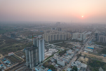 Fototapeta na wymiar aerial drone shot passing over a building with homes, offices, shopping centers moving towards skyscapers in front of sunset showing the empty outskirts of the city of gurgaon