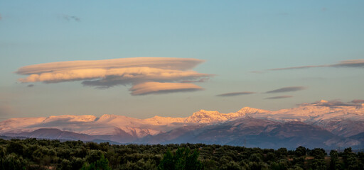 Lenticular clouds over snowy mountains at sunset