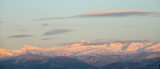 Naklejka premium Lenticular clouds over snowy mountains at sunset