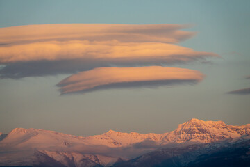 Lenticular clouds over snowy mountains at sunset