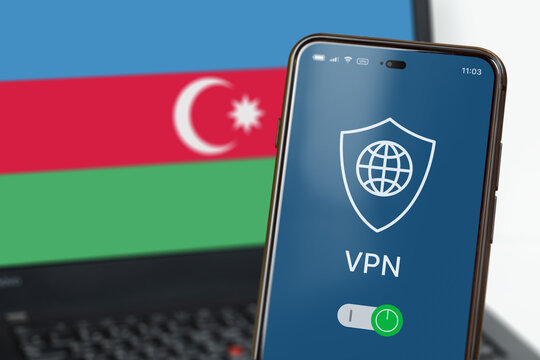 A smartphone with VPN turned on in the foreground and a laptop with the Azerbaijani flag on the screen in the background. Using VPN in Azerbaijan. VPN on cell phone and computer. Selected focus - Powered by Adobe