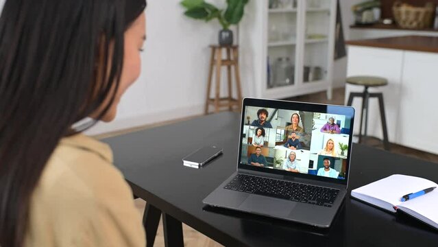 Video meeting, online conference with coworkers. Young woman is using laptop app for video communication with several people together while sitting at the table at home