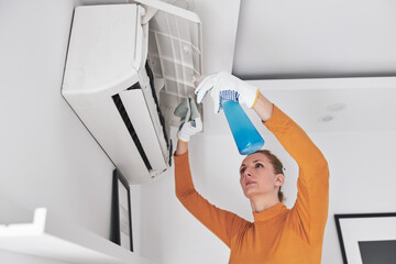 Woman cleaning aircon filters indoor unit at home.