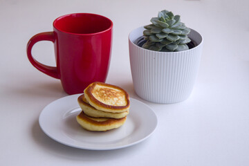 Fresh fluffy homemade pancakes on the plate, red mug and succulent plant on a table