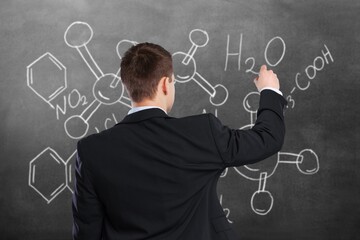 A smart scientist stands at the school blackboard explaining  scientific formulas